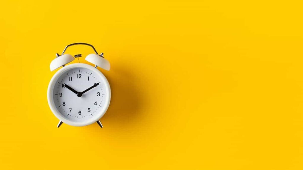 a-white-old-fashioned-clock-against-a-yellow-background.